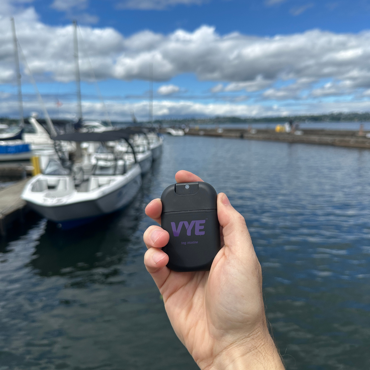 A hand holding VYE mist with boats and water in the background