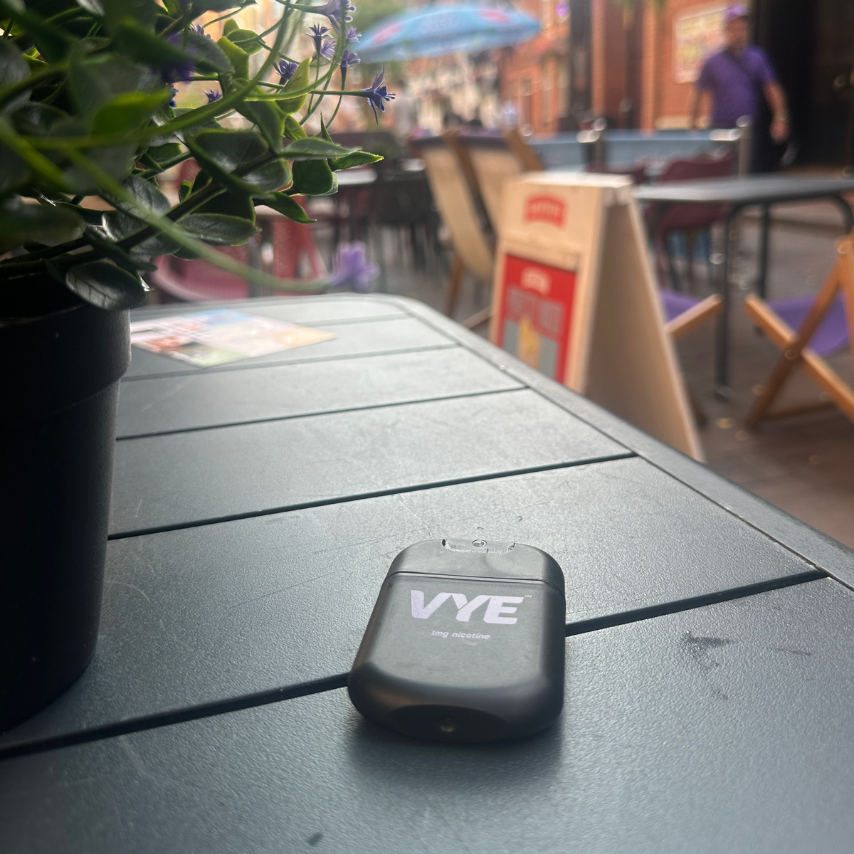 VYE mist on a café patio table with a plant and the street beyond