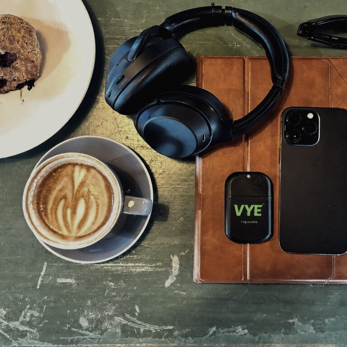 VYE mist beside headphones, coffee, and a phone on a café table